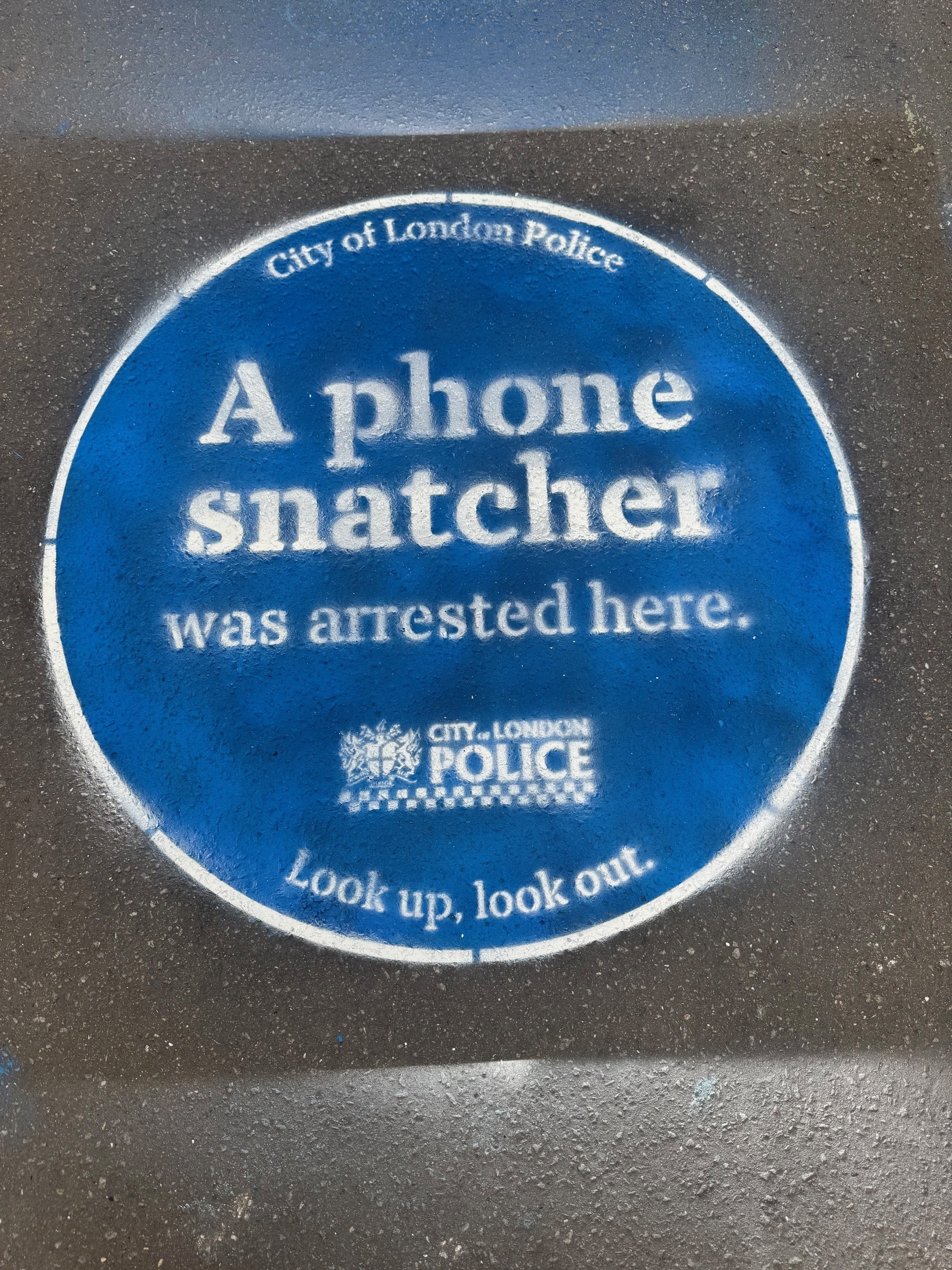Spray painted blue plaque with words 'a phone snatcher was arrested here'